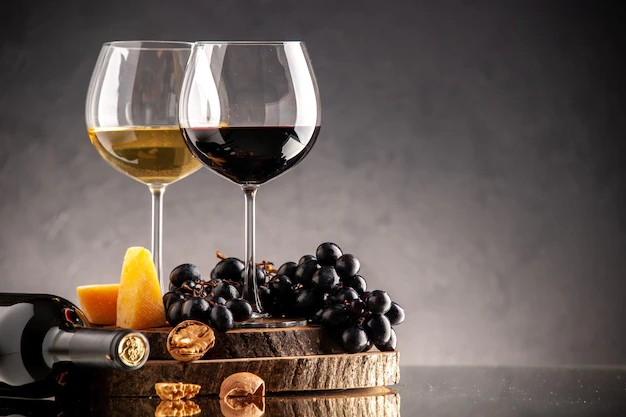 Free Photo | Front view wine glasses fresh grapes walnuts yellow cheese on wood board overturned bottle on dark background