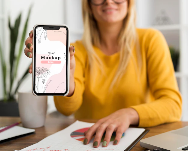 Free PSD | Woman at desk showing phone mock-up