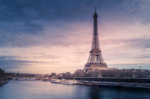 Free Photo | Beautiful wide shot of eiffel tower in paris surrounded by water with ships under the colorful sky