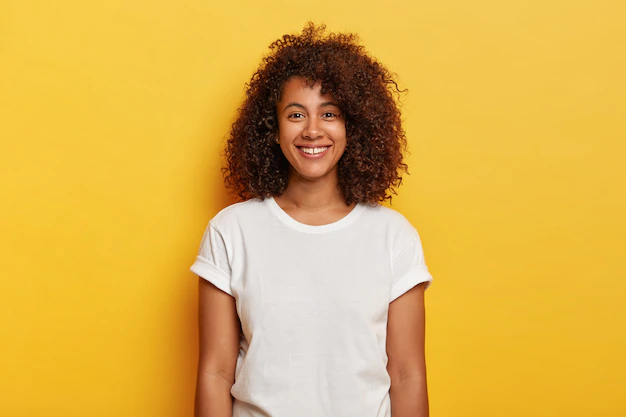 Free Photo | Headshot of beautiful dark skinned curly has pleased expression, rejoices success, enjoys spare time, wears casual t shirt, isolated on yellow wall. people, positive emotions, feelings concept